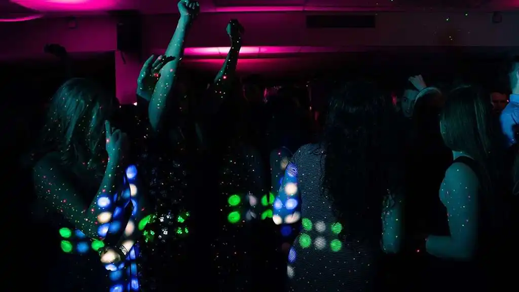 Darkened room with lots of young people dancing at a disco